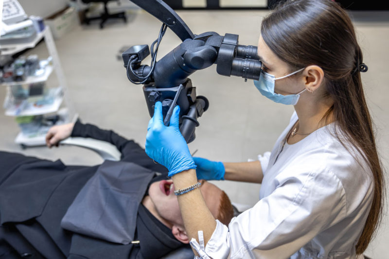 tanara stomatolog care trateaza dintii pacientului cu microscopul dentar