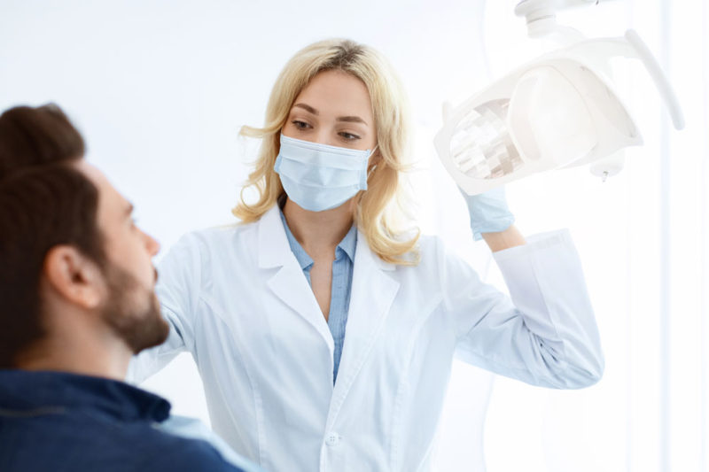 Dentist cu masca de fata salutand pacientul