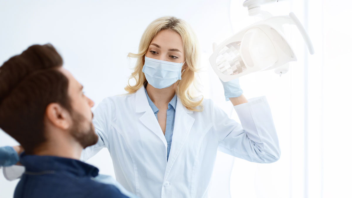 Dentist cu masca de fata salutand pacientul