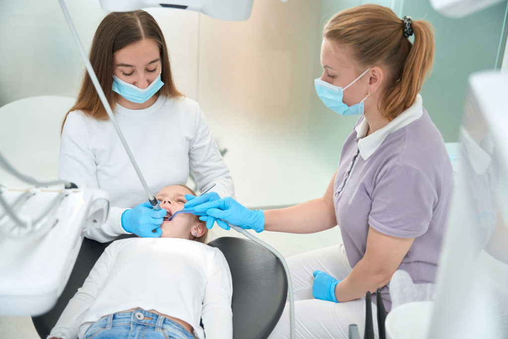 Pedodont care trateaza cariile la o fetita asistata de asistenta
